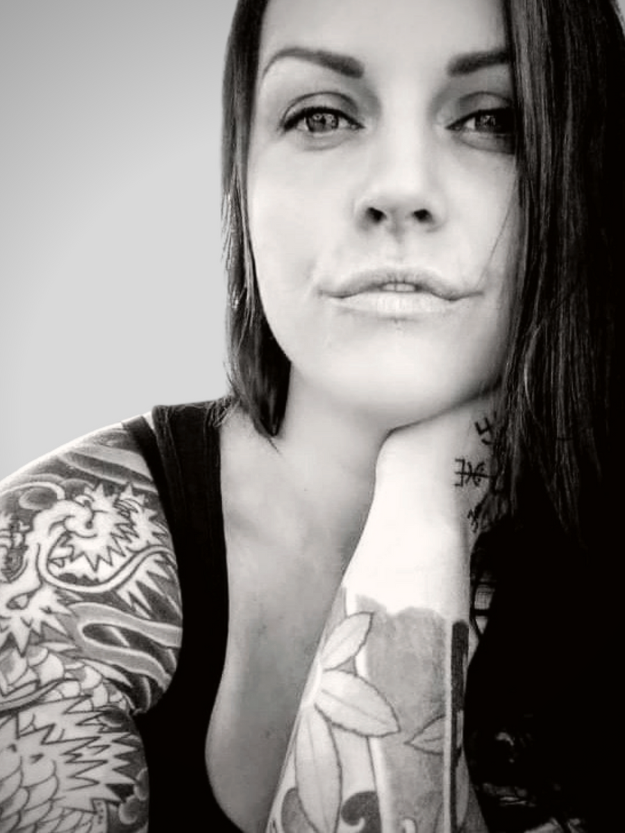 Artist Jess Alice black and white portrait photo. Woman with hard hair, light eyes, tattoos. Neutral facial tone, get to know more about the artist, and access social media links to facebook, instagram, tiktok, pinterest youtube